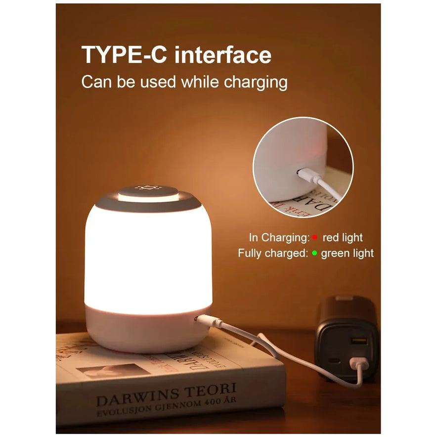 The Touch Control LED Night Light Lamp, USB rechargeable with Type-C, sits on books emitting warm light. Close-up: charging port shows In Charging: red light, Fully charged: green light. A plugged-in charger nearby enhances its modern convenience for bedside or desk use with 3 color settings.