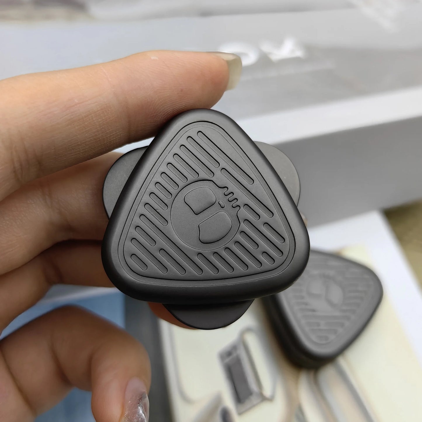 A hand holds a small, black EDC Fingertip Toys Fidget Slider—a magnetic metal decompression spinner with a raised pattern. Another is blurred in the background, highlighting its sleek design and fine craftsmanship.