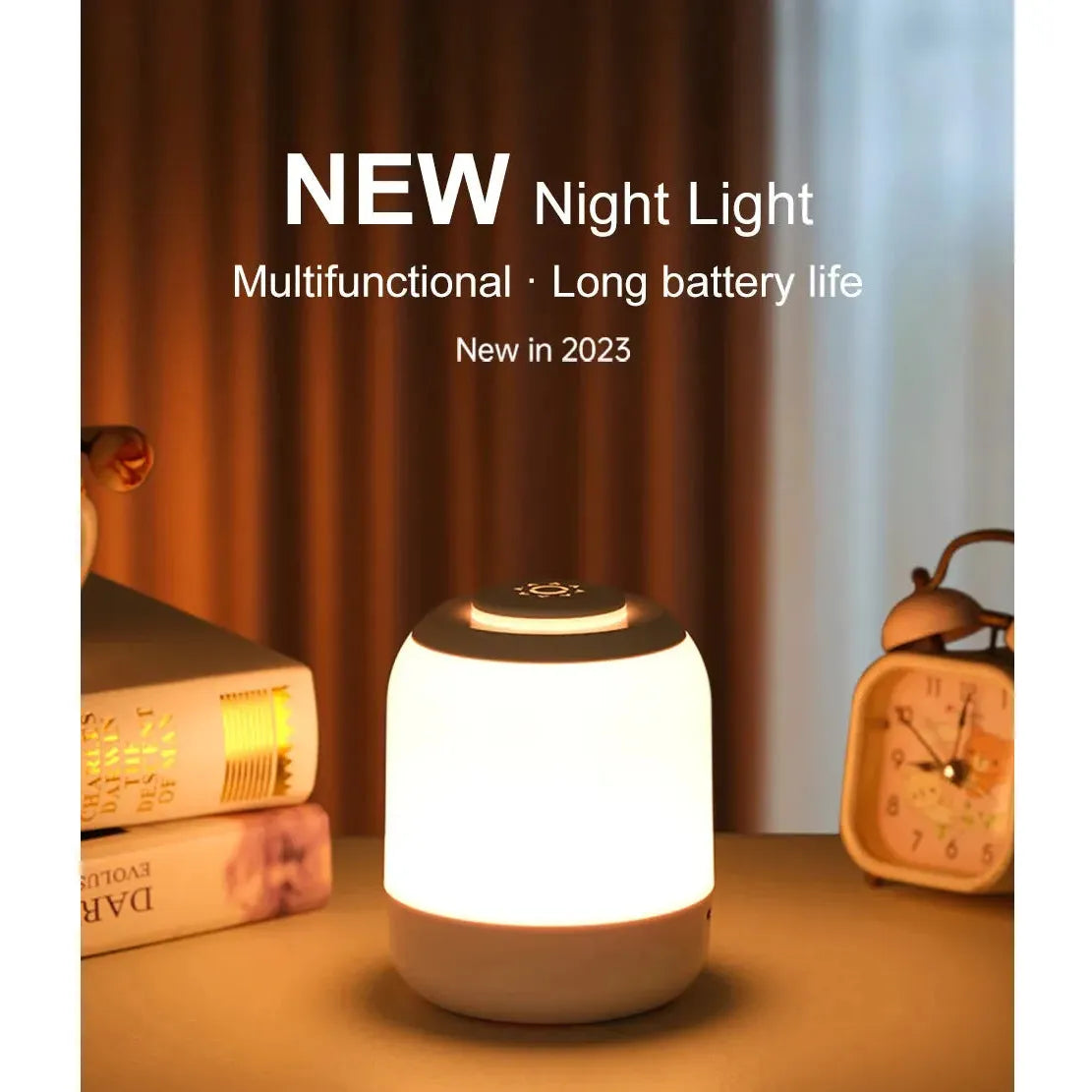 A softly glowing LED table lamp with touch control and three color settings sits on a table beside stacked books and a vintage-style alarm clock. Text above reads: NEW Night Light, USB Rechargeable, Portable Desk Lighting, New in 2023. Curtains partially visible in the background.