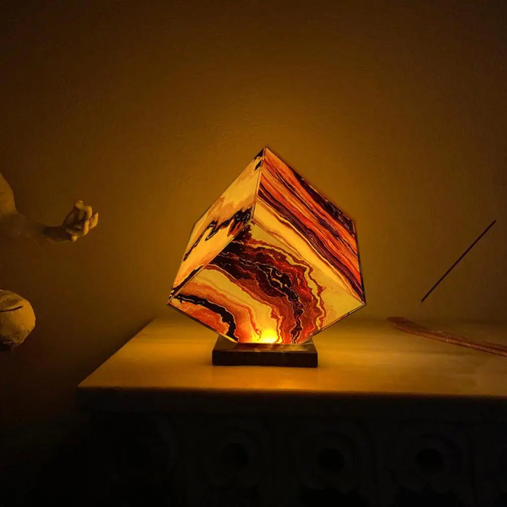 The Elegant Agate Crystal Table Lamp, with marbled orange-brown patterns, emits warm ambient light on a table. Paired with a hand sculpture and incense stick, it enhances the artistic design, making it an ideal bedside decor lamp.