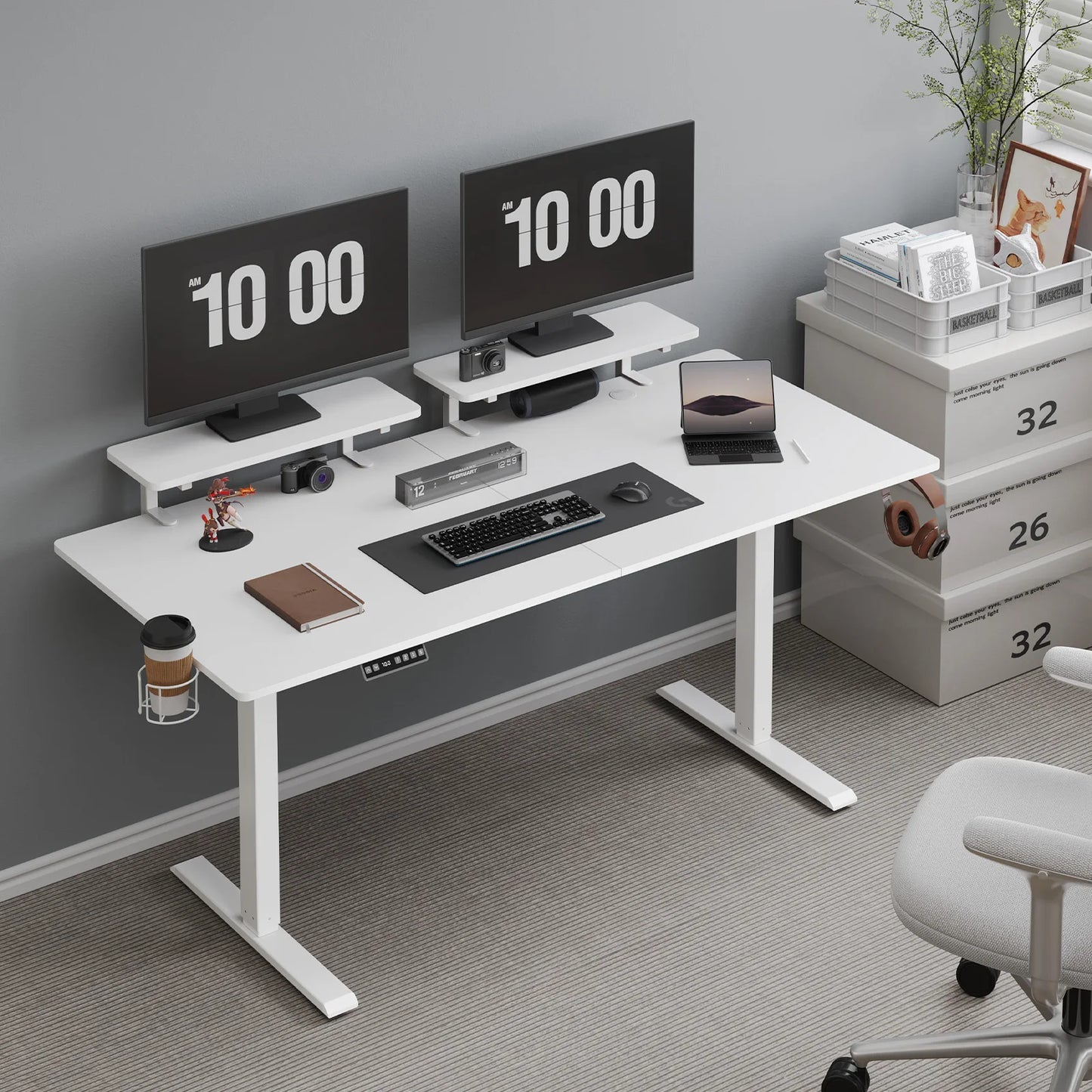 A 63-inch white Standing Desk w/ 2 Adjustable Monitor Shelves Electric Stand Up Desk features dual monitors showing “10:00,” keyboard, mouse, laptop, camera, plants, and office supplies. White drawers labeled 32 and a chair sit on light gray carpet nearby.