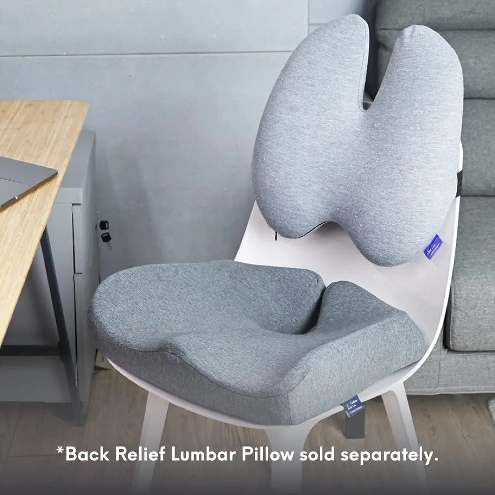 A wooden desk hosts a white chair with a Cushion Lab Patented Pressure Relief Seat Cushion and memory foam backrest. Near the plush grey sofa, it combines comfort and style. Note: *Back Relief Lumbar Pillow sold separately.