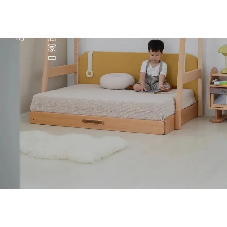 A child sits on the Versatile Solid Wood Childrens Bed with Climbing Frame and Swing, adorned with a mustard yellow backrest, playing with a toy. In the room, theres a light fluffy rug and a small bookshelf accompanied by a yellow lamp.