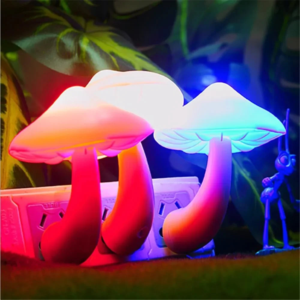 Three Mushroom LED Night Lights with sensor control plug into the wall, emitting warm white hues. Nearby, a small blue plastic figure adds to the whimsical ambiance against green foliage.