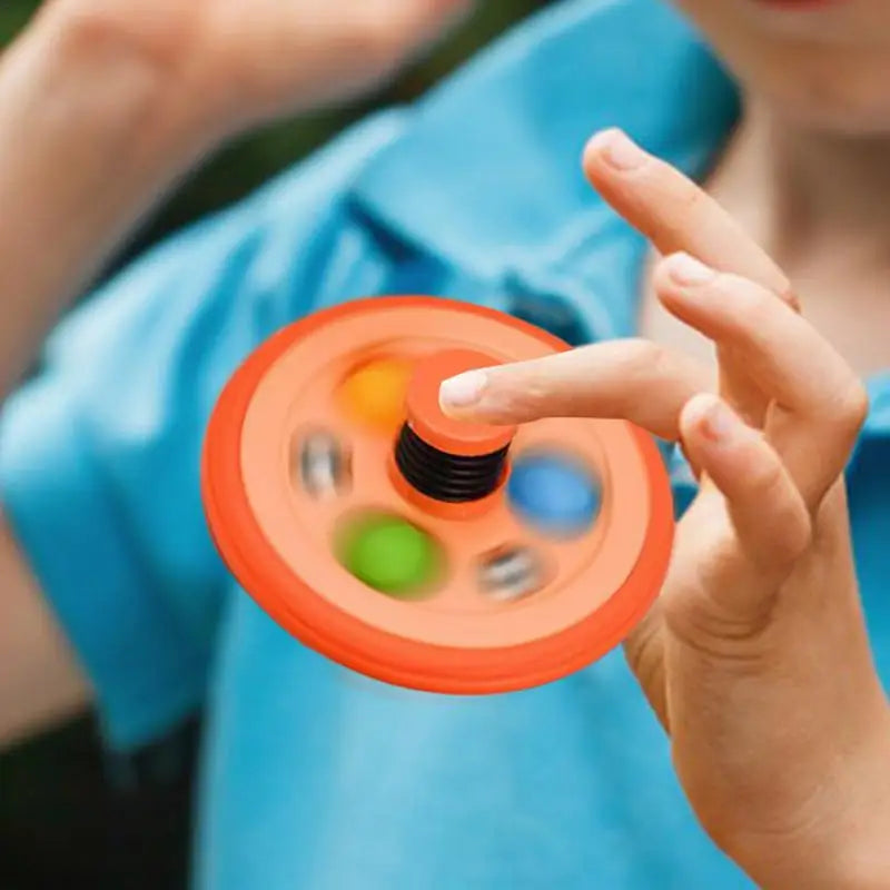 A child in a blue shirt spins a Pop Fidget Toy Gyro, an orange fidget gyroscope with colored circles and spring mechanism rubber tire, popular as birthday and classroom prizes across Mainland China.