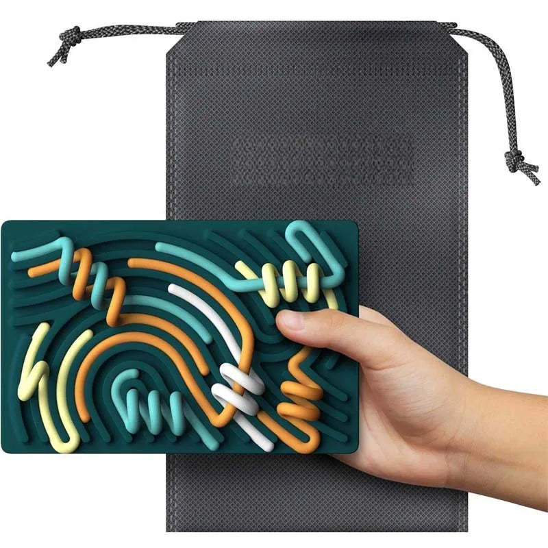 A hand holds a green Childrens Puzzle Silicone Sensory Activity Board made of food grade, BPA-free silicone, with colorful winding tracks. A textured black drawstring pouch is shown in the background.