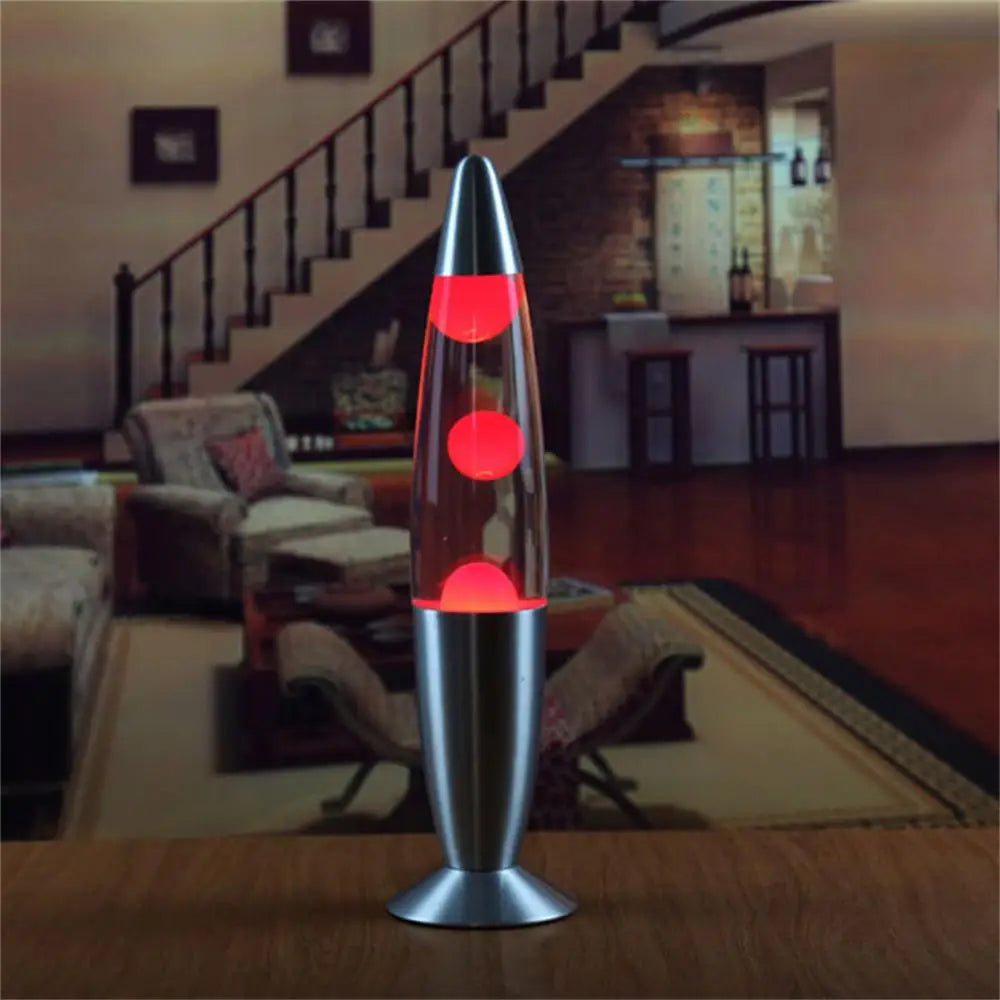 The Mesmerizing Jellyfish Lava LED Night Light in red sits on a wooden table in a cozy living room, enhancing the warm ambiance with its decorative aluminum alloy build against a backdrop of stairs, wall art, and comfortable seating.