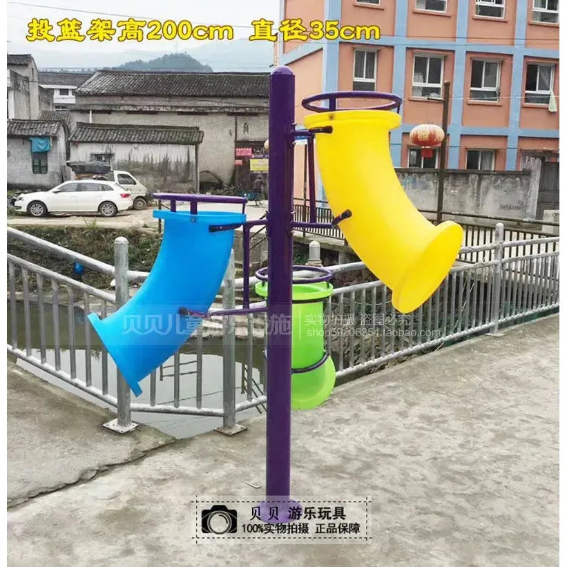 The Outdoor Steel Climbing Frame Swing for Childrens Sensory Integration Training features blue, yellow, and green funnel-shaped tubes attached to a purple pole. The vibrant scene includes buildings and a river with a bridge in the background.