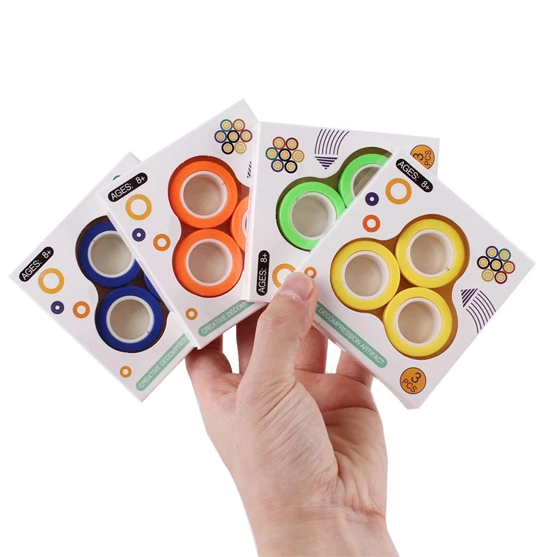 A hand holds three packs of Finger Magnetic Rings Fidget Toys for Anxiety, ADHD, and Stress Relief—each set in white boxes with colorful circular designs. Perfect for creative projects or as a stress relief fidget gadget.