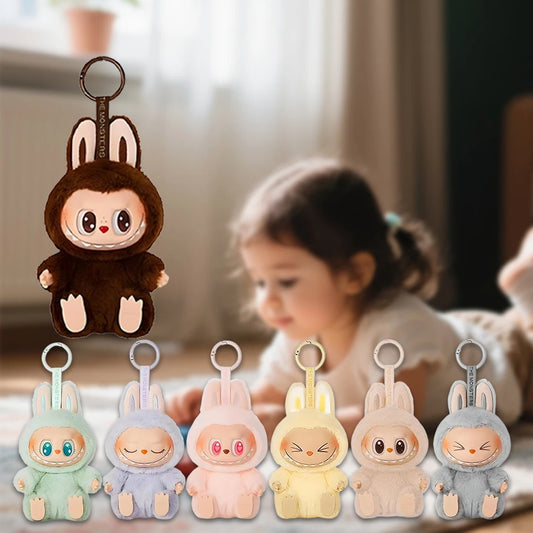 A young child relaxes indoors on a soft carpet, surrounded by six MINISO Cute Labubu The Monsters Box Toy Sweetheart Vinyl Doll backpack pendant plush keychains, each with big eyes and animal ears; one plush hangs prominently in the foreground.