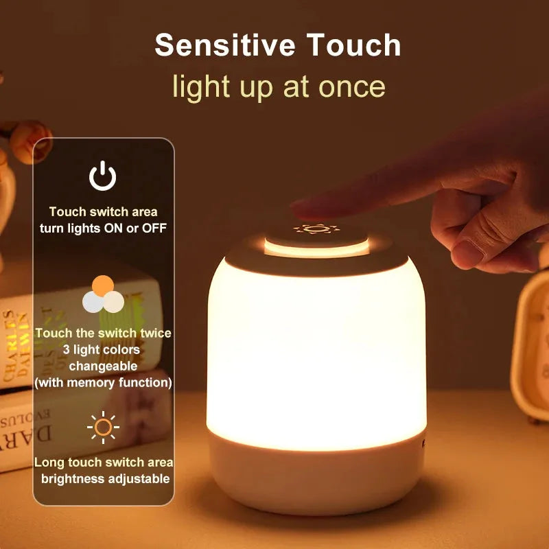 In a blurred nightstand setting, someone interacts with the USB rechargeable Touch Control LED Night Light Lamp, adjusting its color and brightness using touch sensor controls. The lamp offers 3 color settings for versatile bedside or desk lighting for kids and babies.