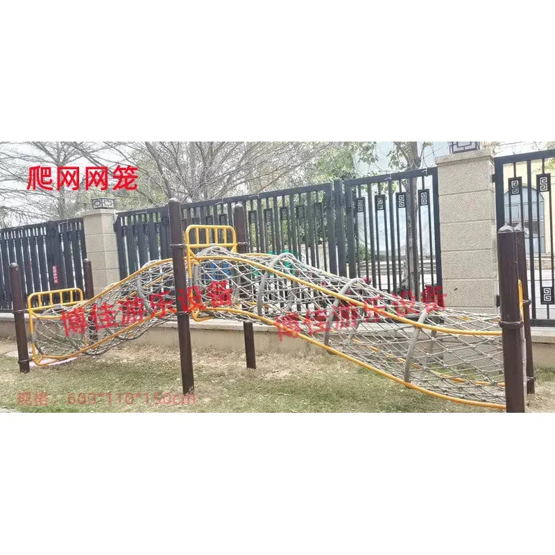 The childrens playground includes wavy rope nets for climbing framed by yellow and brown bars, ideal for kids aged 3-8. Its set on grass with a sturdy metal fence and trees, featuring red text on the image. Part of the outdoor toys line for sensory integration and physical training sports equipment.
.