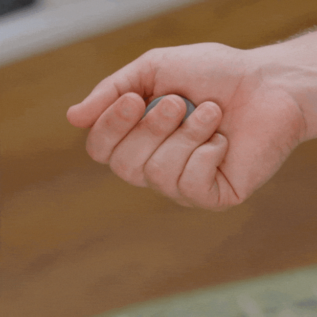 A hand repeatedly squeezes the ONO Scroller Titanium, a small gray fidget stress ball, demonstrating how it changes shape under pressure from the fingers.