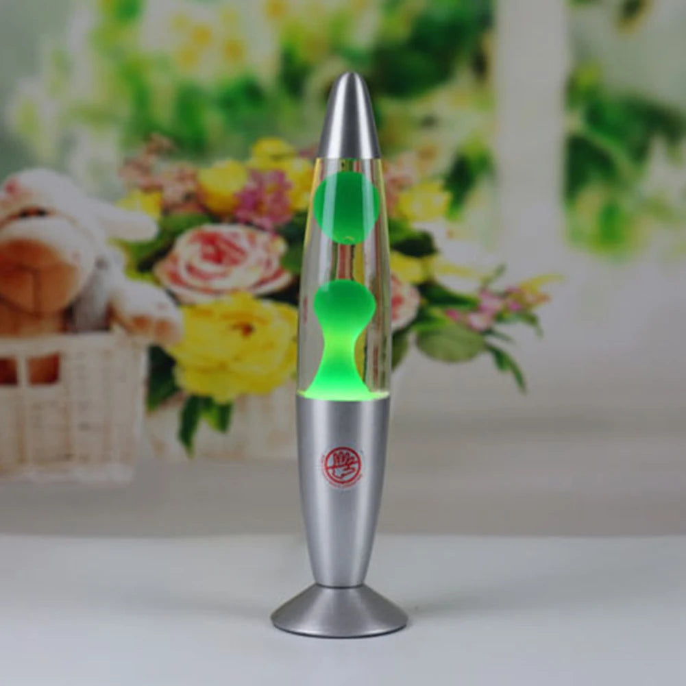 The Luminous Volcano Lava Jellyfish LED Night Light, a creative 25W atmosphere lamp, enhances relaxation with its silver design and green wax on a table, while blurred flowers like soft-colored roses add a decorative touch in the background.
