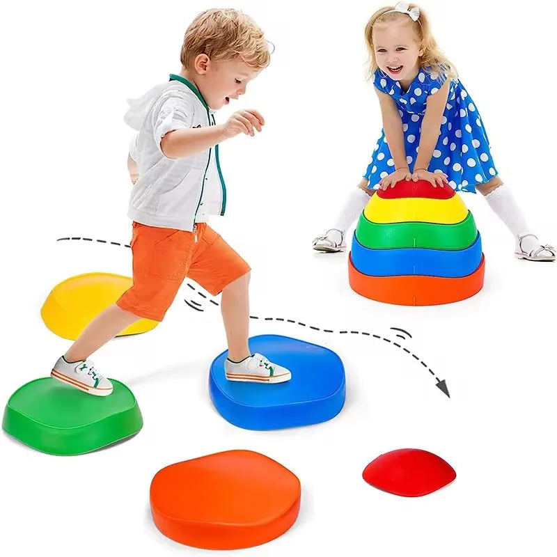 A young boy and girl develop motor skills on Adventure Balance Stones, a tactile sensory stepping kit. The girl in a blue polka-dot dress and the boy in orange shorts practice balancing on the vibrant red, orange, yellow, green, and blue stones arranged in a path.