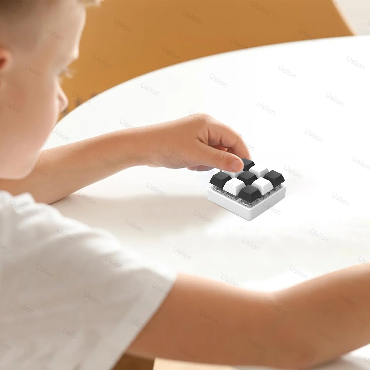 A child sits at a white table, focusing intently on adjusting the pieces of a 9 Keys Keyboard Key Toy DIY Fidget Button Keycap, enjoying the stress relief it provides.