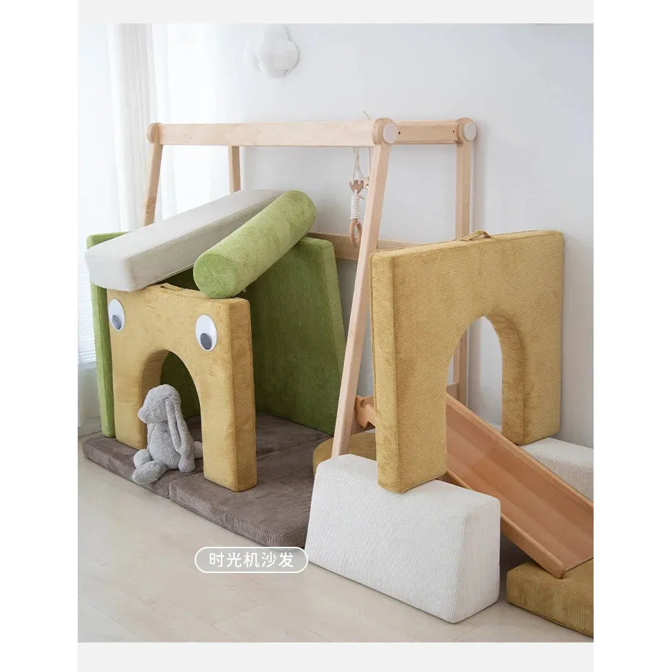 A childrens play area includes a Versatile Solid Wood Childrens Bed with a climbing frame, swing, and house-themed soft, colorful cushions and blocks. It features green, beige, and brown tones with large googly eyes on one cushion, plus a slide and plush toy rabbit for added fun.