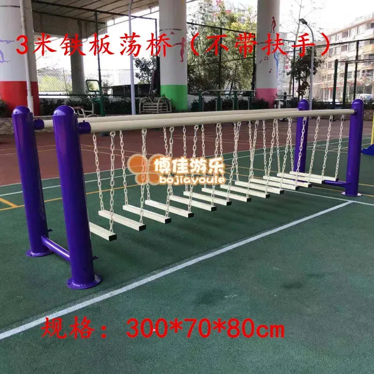 An outdoor sports surface installation includes a balance beam with suspended wooden planks on chains, framed by 3-meter iron posts. This component of the childrens swings and sensory integration setup features accents in red and white for an engaging physical training experience.