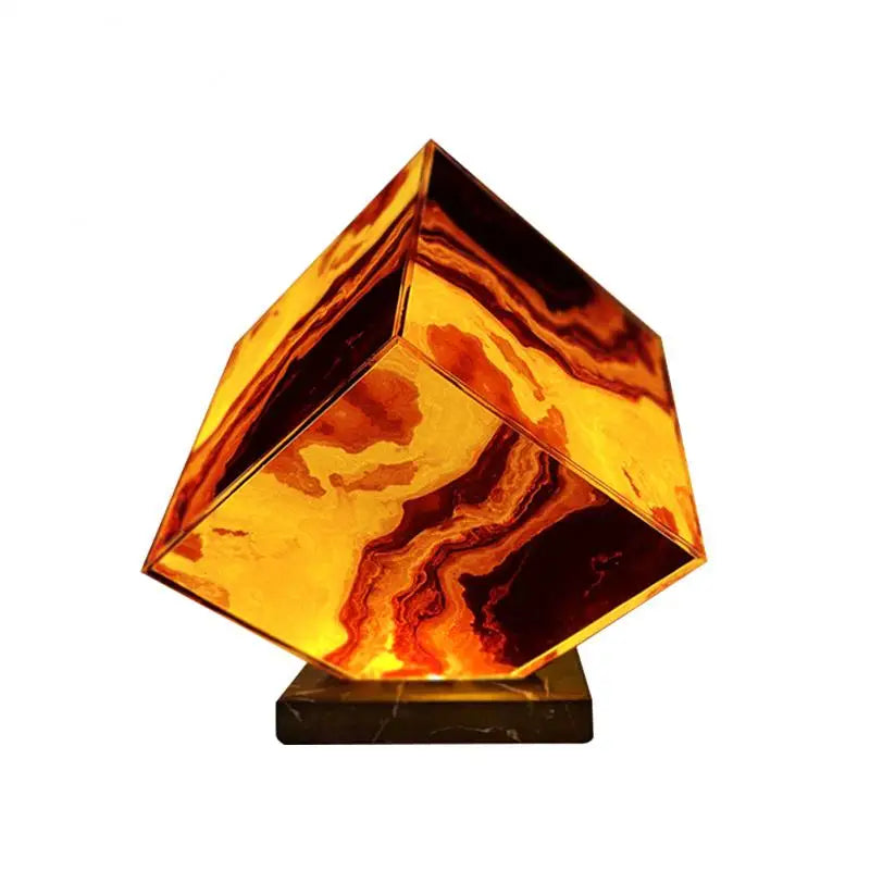 The Elegant Agate Crystal Table Lamp, with a glowing cube-shaped shade in swirling amber, orange, and brown hues on a dark base, resembles an agate crystal. It casts warm light highlighting the marbled pattern, making it perfect for bedside décor.