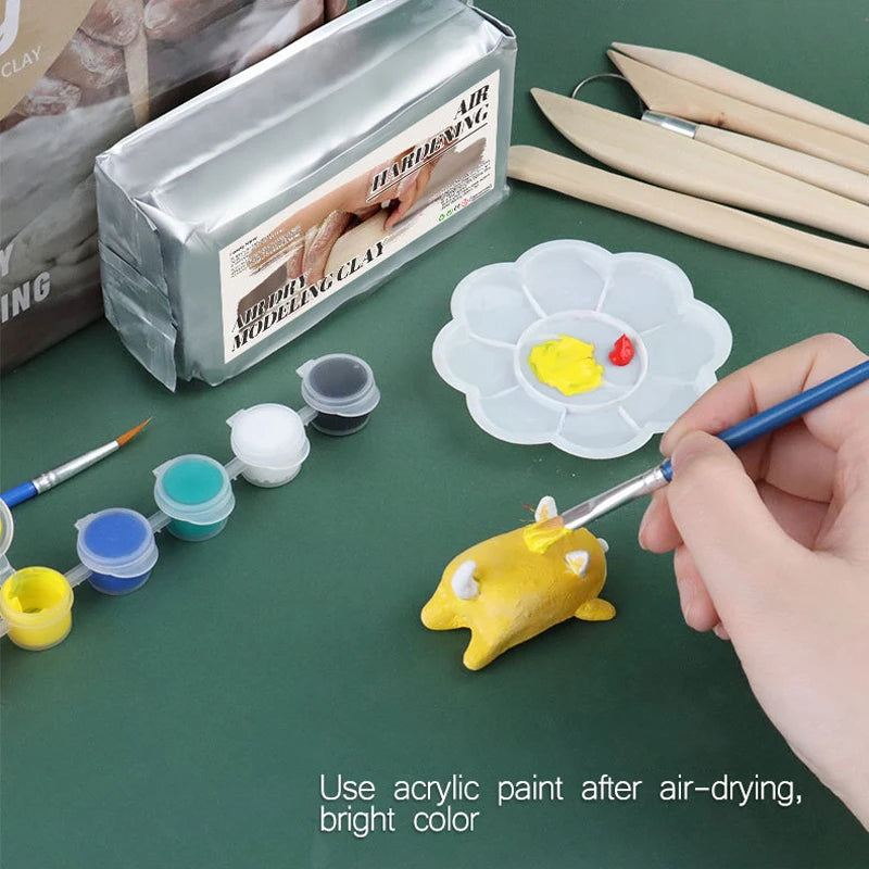 Using the No-bake Air-dried Shaping DIY Plasticine Clay Set, a person paints a small yellow clay animal with acrylics and a brush. Surrounding them are various colors, wooden tools, and a palette. Instructions suggest using acrylic paint post air-drying for vibrant color—no baking required.