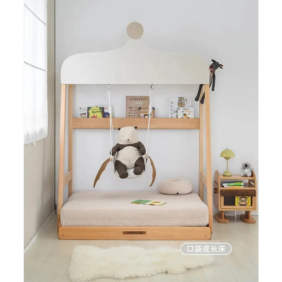 A childrens room showcases the Versatile Solid Wood Childrens Bed with Climbing Frame and Swing Features, accompanied by a small bedside table holding a lamp and books. A plush rug covers the floor, and stuffed animals decorate the swing. Natural light from a large window enhances the cozy space.