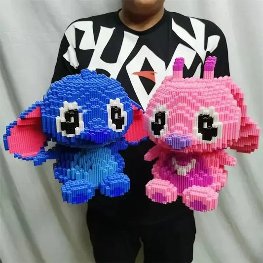 A person holds two Large Stitch Building Block Assembly Toys, each 30cm tall; one is blue with pink ears, the other pink with heart details. Both have big eyes and are made of stacked rectangular building blocks.