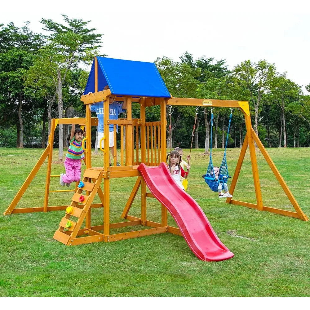 Three children, aged 3-6, enjoy a Wooden backyard swing set in amber yellow with a colorful canopy, slide, climbing wall, sandbox, and two swings. The playset stands on grass with trees in the background.