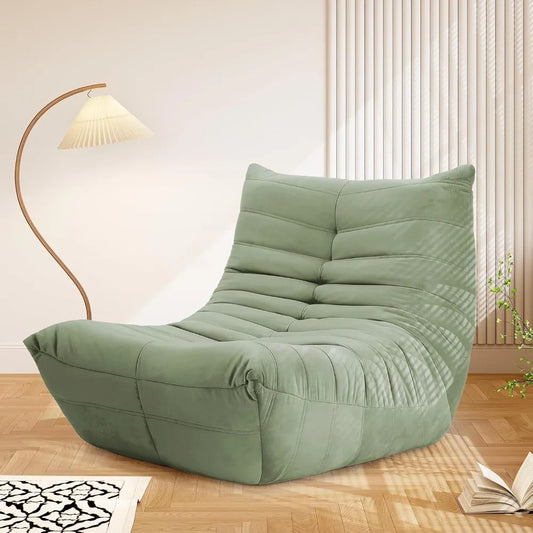 A modern green Fireside Chair Bean Bag for adults with cozy memory foam fill sits on a wooden floor beside a curved floor lamp, sunlight streaming through blinds and an open book nearby.