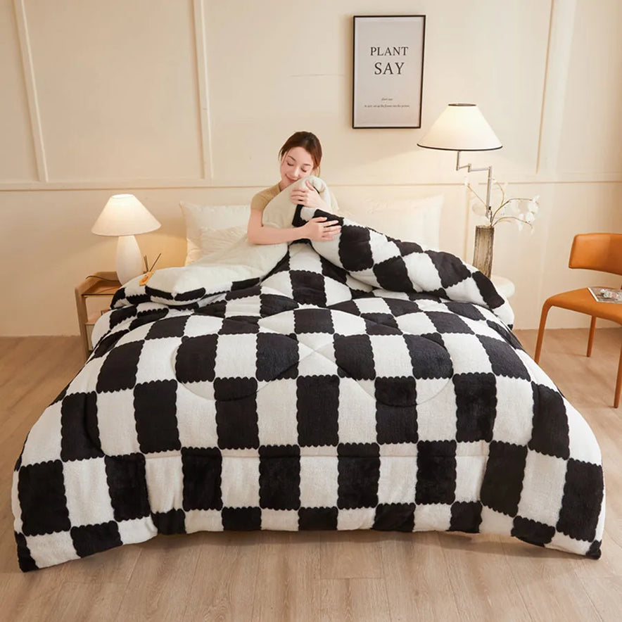 A person sits on a bed with the KDJEIKZ Ultra Cozy Winter Weighted Blanket, its milk velvet texture adding a cozy touch. The bedroom features beige walls, two lamps, a brown chair, and a small framed quote. Light wood floors complete the rooms serene ambiance.