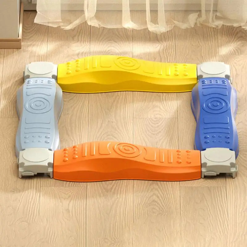 The Sensory Balance Beam Training Board for Kids forms a square path with four interlocking beams in yellow, blue, orange, and light blue. Designed for motor skills development, they rest on a light wood floor near a window with a sheer curtain.