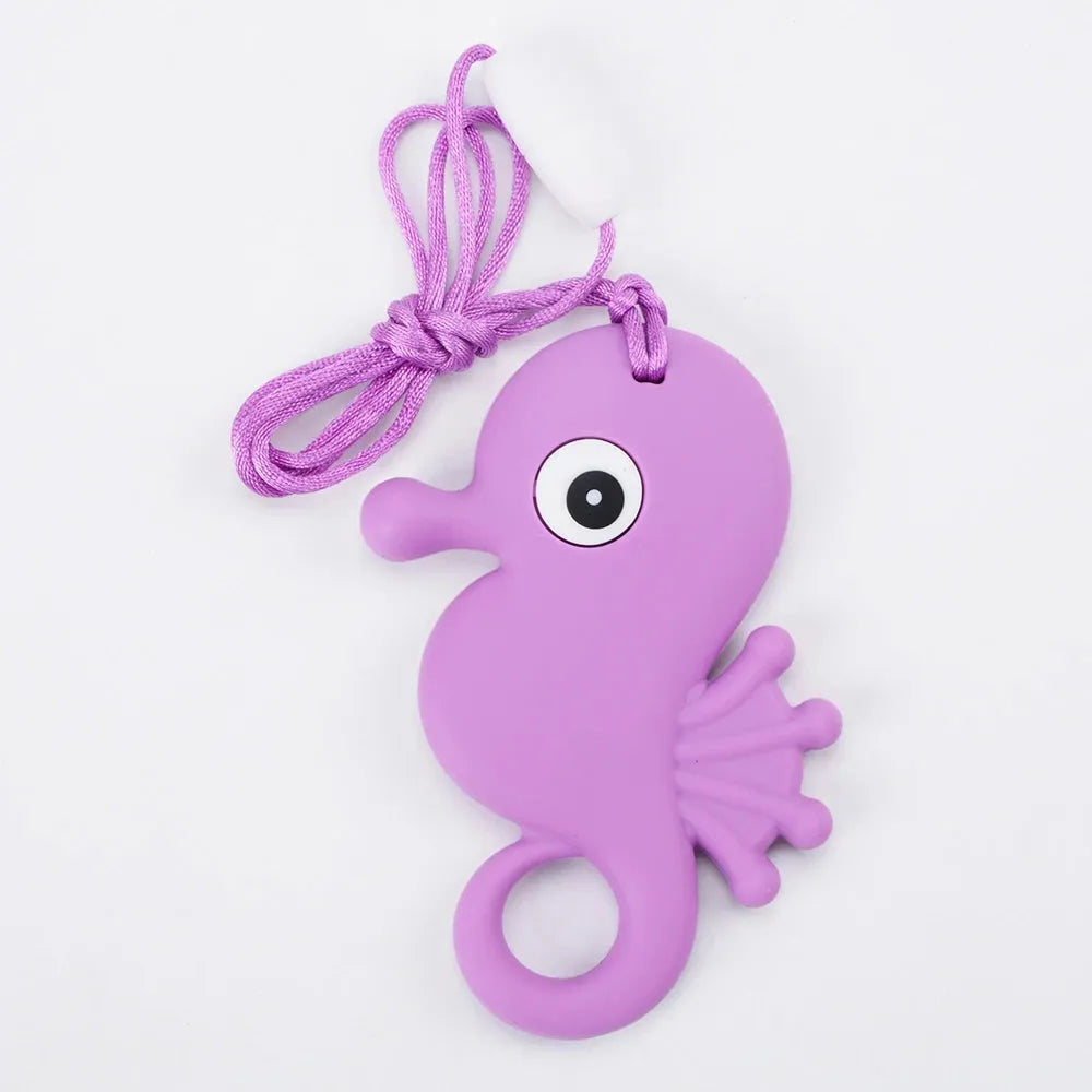 The Silicone Chewable Necklace for Kids, shaped like a purple seahorse with a smooth texture and large eye, comes with an attached purple string. Ideal for autism and ADHD therapy, this sensory teether pendant rests stylishly on a white background.