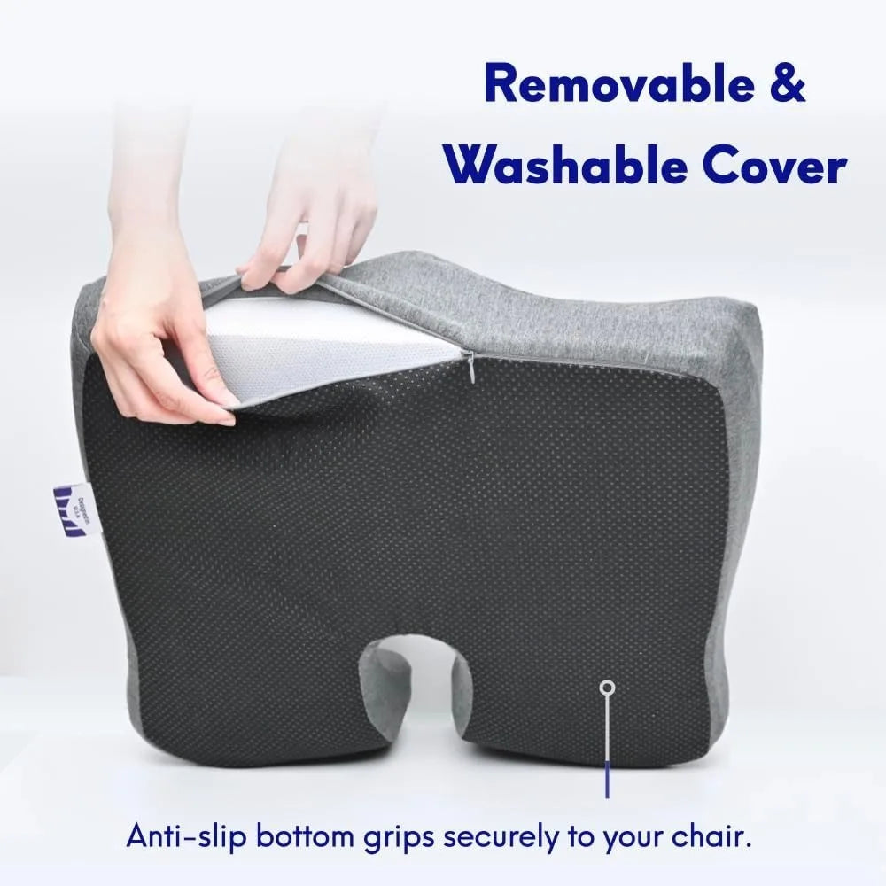 A gray memory foam seat cushion with a cutout is shown being unzipped by a hand to reveal its 100% cotton removable cover. It features an anti-slip bottom. Blue text reads Removable & Washable Cover and Anti-slip bottom grips securely to your chair.