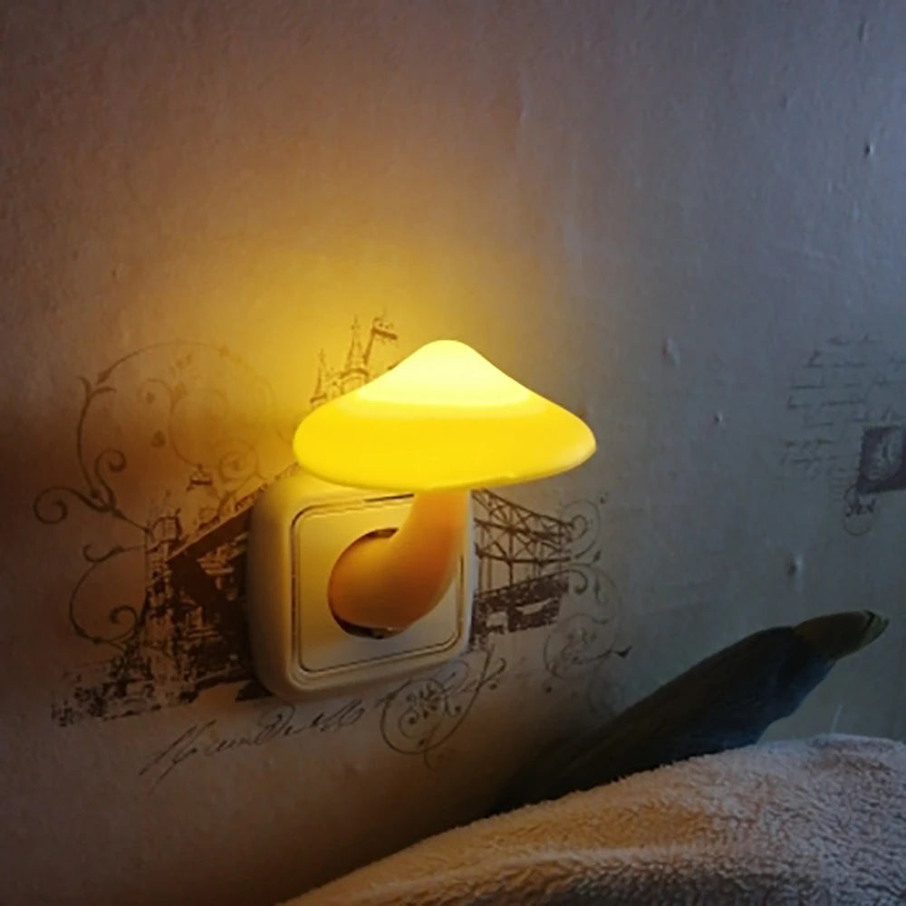 The Mushroom LED Night Light with Sensor Control, plugs into an EU/US socket and emits a warm white glow with decorative patterns. A glimpse of the bed pillow in the foreground enhances the cozy ambiance.