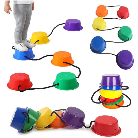A child in gray pants and white shoes explores sensory integration on Montessori Colorful Balance Stones for Sensory Play and Developmental Training, balancing on red, yellow, green, blue, orange, and purple stones connected by ropes while some are stacked aside.