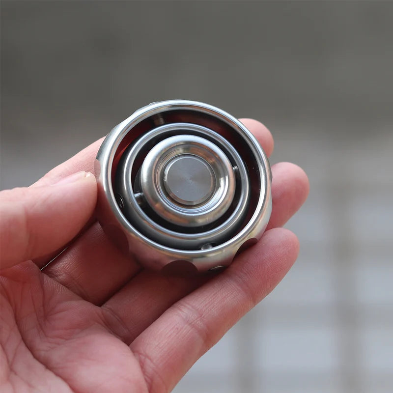 A hand holds a sleek Stainless Steel Fidget EDC Gyroscope Spinner, designed for stress relief and featuring concentric rings with a central button, set against a blurred neutral background.