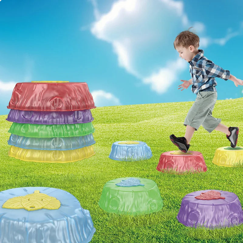 A child in a plaid shirt joyfully hops across Rainbow Luminous Balance Stones for Kids, shaped like tree stumps on a grassy field under a blue sky with clouds, while nearby, more stones await outdoor tactile balance training adventures.