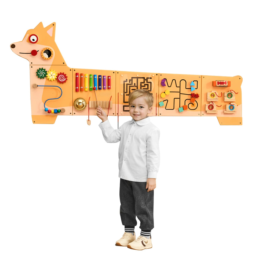 A young child smiles in front of the Vevor Puppy Kids Wall Busy Panels Montessori Sensory Learning Activity Center, an orange dog-shaped board with 12 activities like gears, xylophone bars, mazes, and beads to boost motor skills.