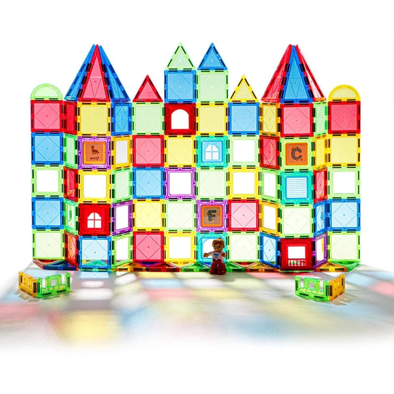 A vibrant castle made from the Magplayer Magnetic Building Blocks Construction Set displays diverse geometric shapes. A tiny toy figure stands amid scattered tiles, enhancing creativity in this Montessori-inspired educational toy against a simple white background.
