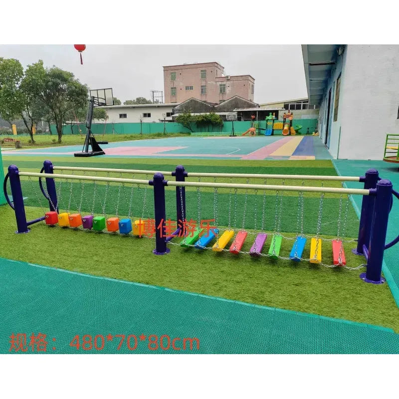 The unisex playground equipment includes a metal toy balance beam with multicolored steps suspended by chains, ideal for ages 3-8. Its located on a green surface near a building, with trees and a basketball hoop visible in the background. Part of outdoor toys and sports equipment range.