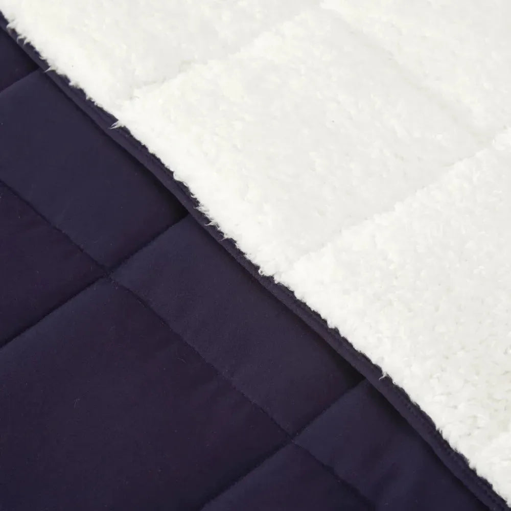 A close-up of the Luxurious Microfiber Weighted Blanket shows quilted fabric with dual textures: one side is super soft and fluffy white sherpa, while the other is smooth dark navy blue. The quilted design perfectly complements its weighted feel on both sides.