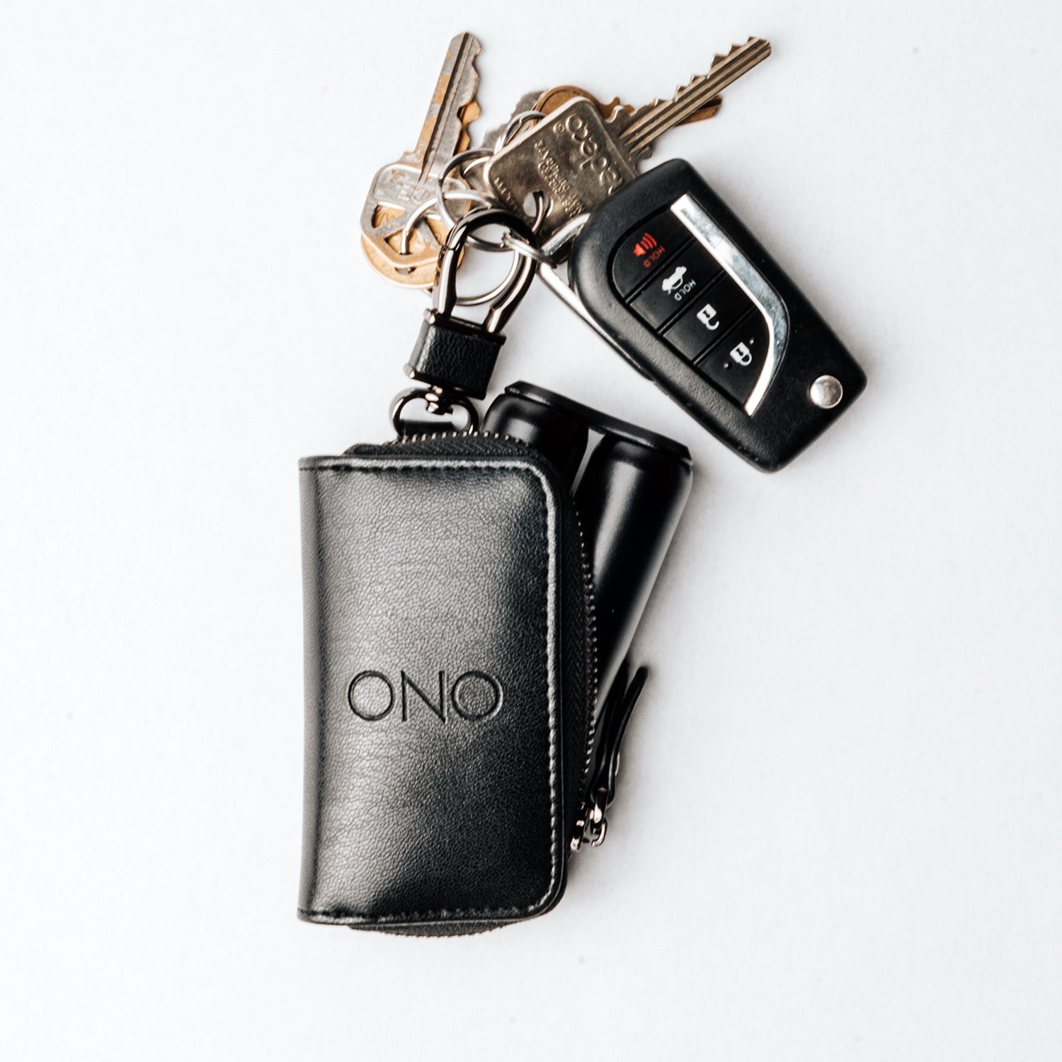 The ONO Roller Premium Keychain Case is a black leather pouch labeled ONO, shown holding a car key fob and several metal house keys on a white background.