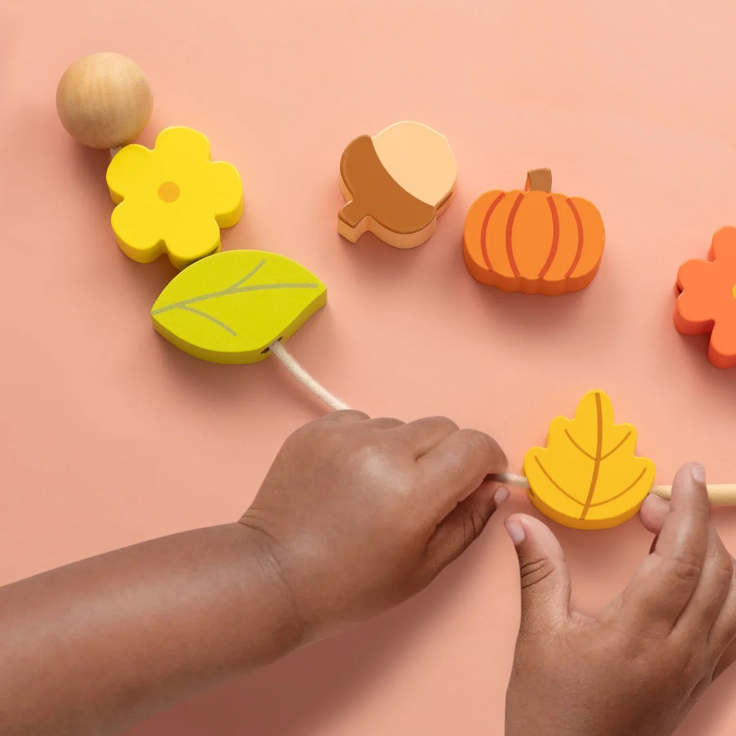 A child threads a yellow leaf bead onto a string with other autumn-themed beads nearby—Tiny Land® Montessori Toys for Toddlers (18–24 Months), perfect for interactive play and fine motor skill development in 2 year olds.