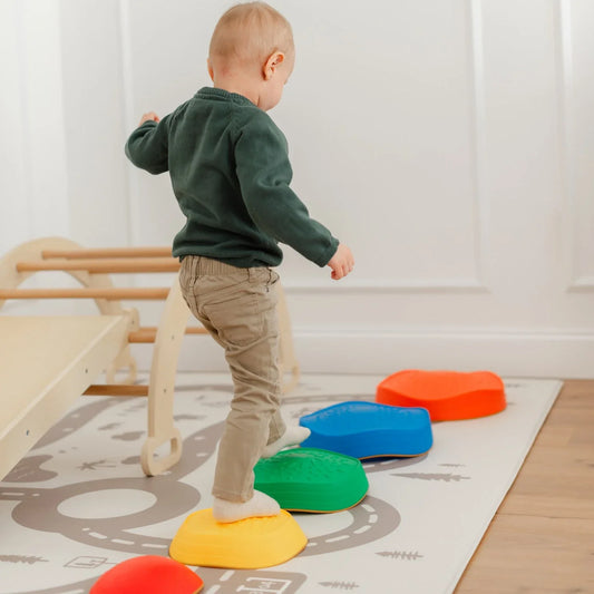 A toddler steps onto colorful, textured Stacking Balance Stepping Stones – Rainbow arranged as an obstacle course on a play mat.