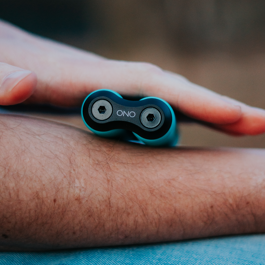 A close-up of a person rolling a blue ONO Roller Soft Touch Plastic on their forearm with one hand, showing its two circular ends and the “ONO” brand name printed between them.