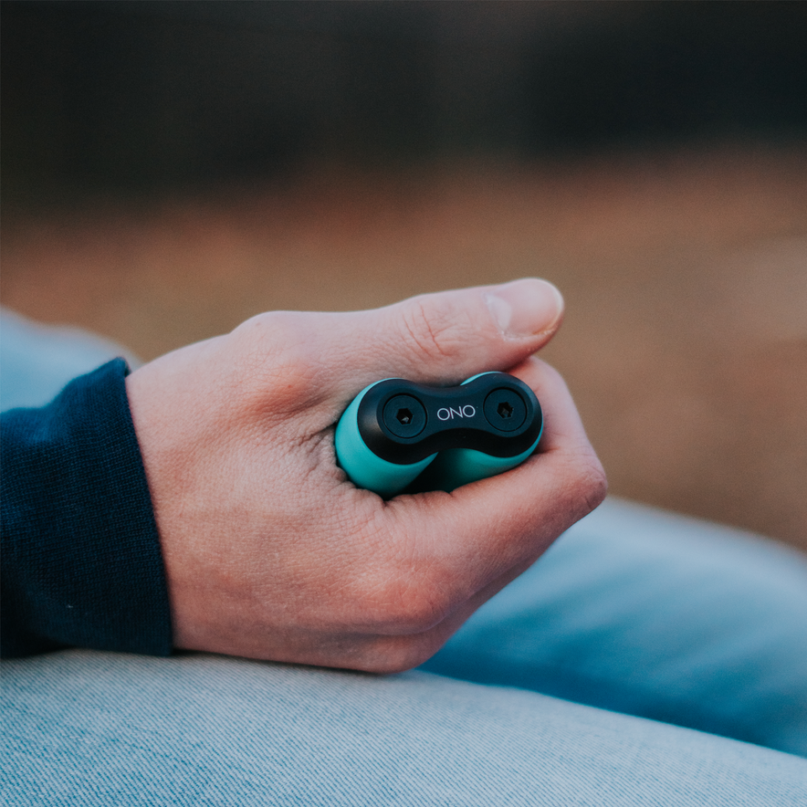 A close-up of a hand holding the ONO Roller Soft Touch Plastic fidget toy for stress relief, with the person in a dark sleeve and light blue jeans, set against a blurred outdoor background.