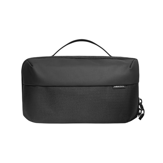 The Tech Pouch is a black rectangular travel organizer with a top handle, minimalist design, and a small front brand tag. The pouch is closed and displayed against a white background.
