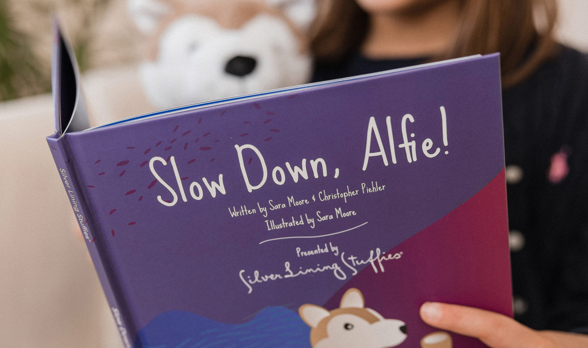 A child holds the Slow Down, Alfie! – Picture Book, which features an illustration of a corgi on its cover.