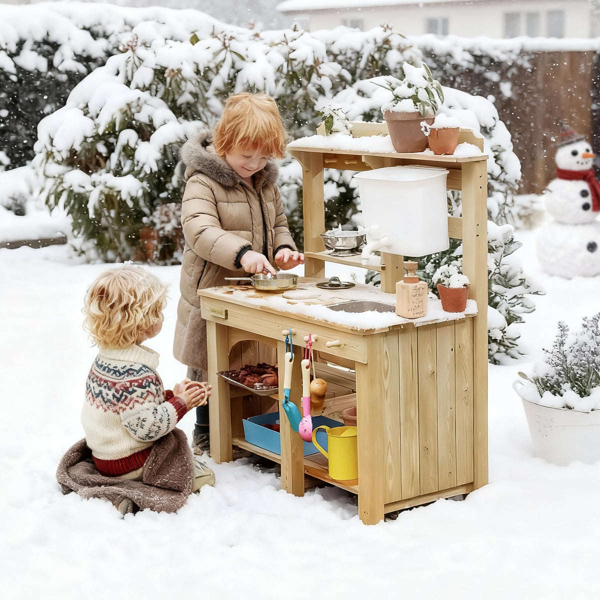 Two children engage in outdoor sensory play with a DuoPlay Outdoor Mud Kitchen with Working Faucet in a snowy backyard.
