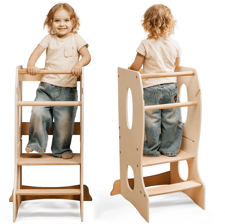 A young child stands on the Stable Montessori Learning Tower: Wooden Growing Chair - Ivory, featuring an adjustable platform, cutout handles, and steps. Shown from front and back, the smiling child wears a beige shirt and blue jeans.
