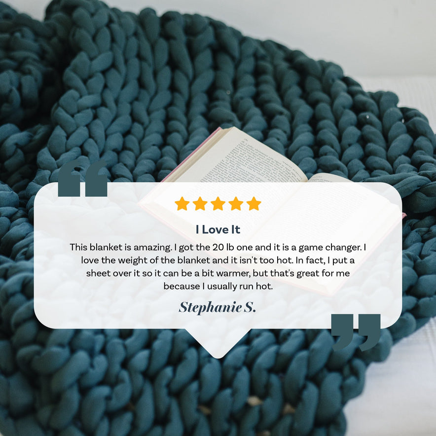 A Knit Weighted Blanket in navy blue is draped on a bed beside an open book. Overlaid is a 5-star review titled I Love It by Stephanie S., praising the blankets weight, comfort, and warmth.